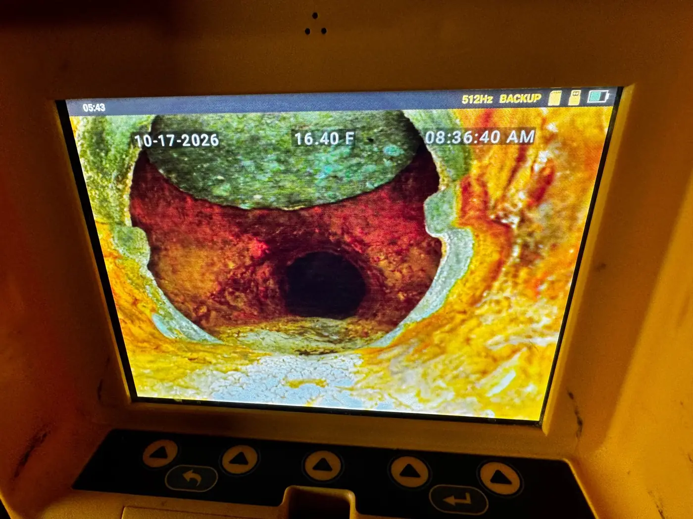Sewer camera view inside a cast iron backwater valve, with the rusted flap sitting raised at the top of the pipe instead of closing across it