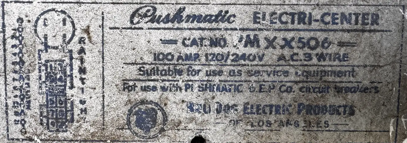 Close-up of a faded stenciled panel label reading Pushmatic Electri-Center, 100 amp, 120/240 volt, suitable for use as service equipment, Bulldog Electric Products of Los Angeles