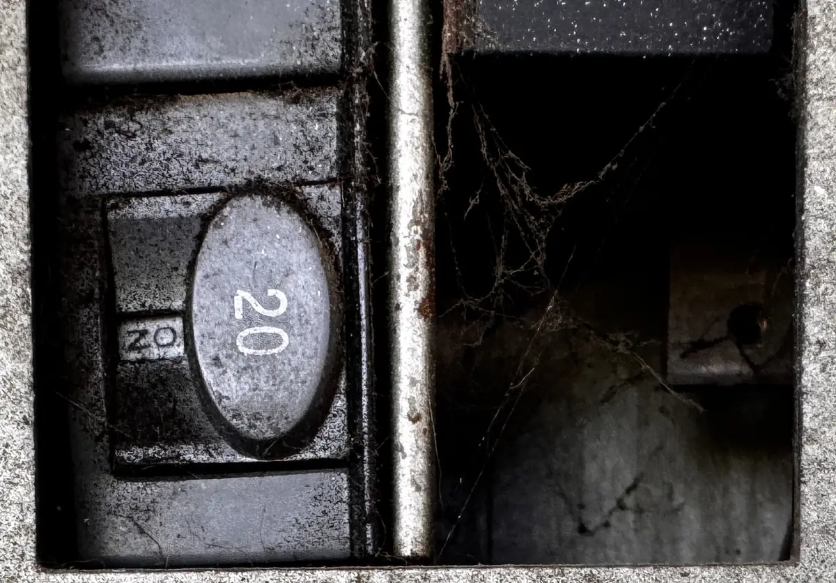Close-up of a 20-amp push-button breaker next to an open breaker space with no filler plate, cobwebs visible inside the panel