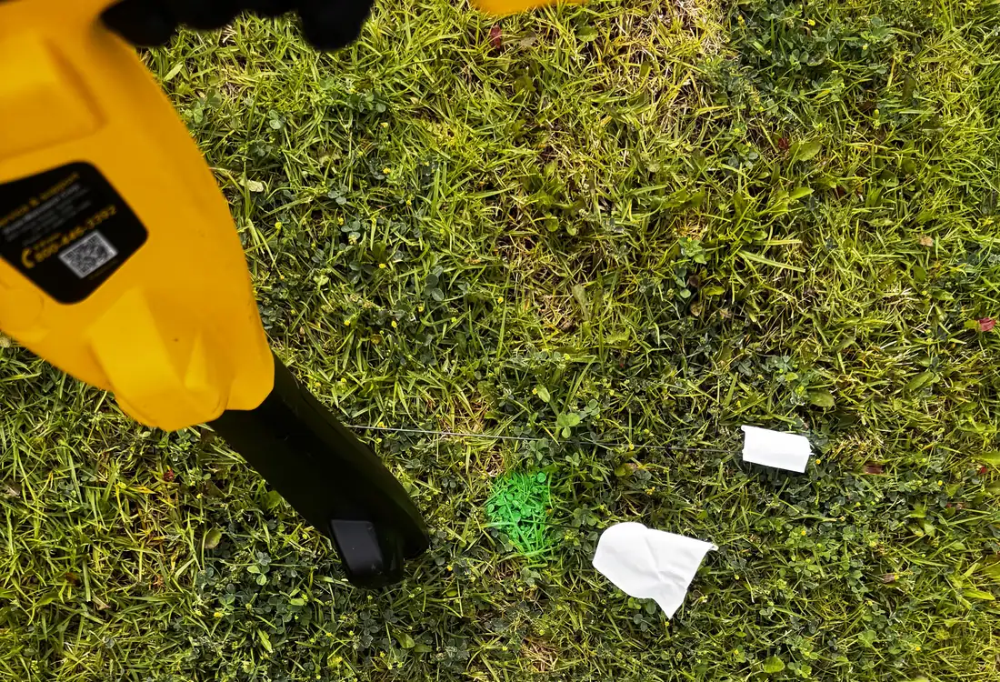 Locator wand tracing the camera head underground, with marker flags placed on the lawn above the line