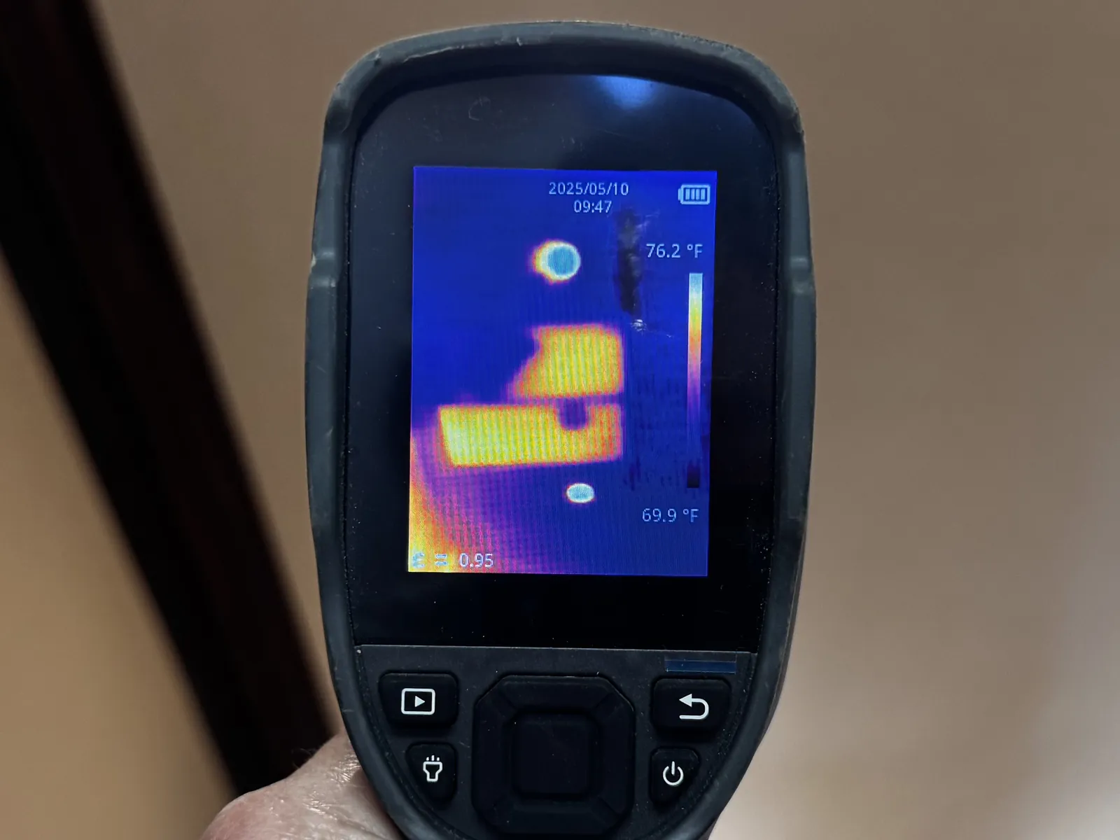 Handheld thermal camera aimed at the same ceiling, its screen showing two bright yellow rectangles against a cool blue background